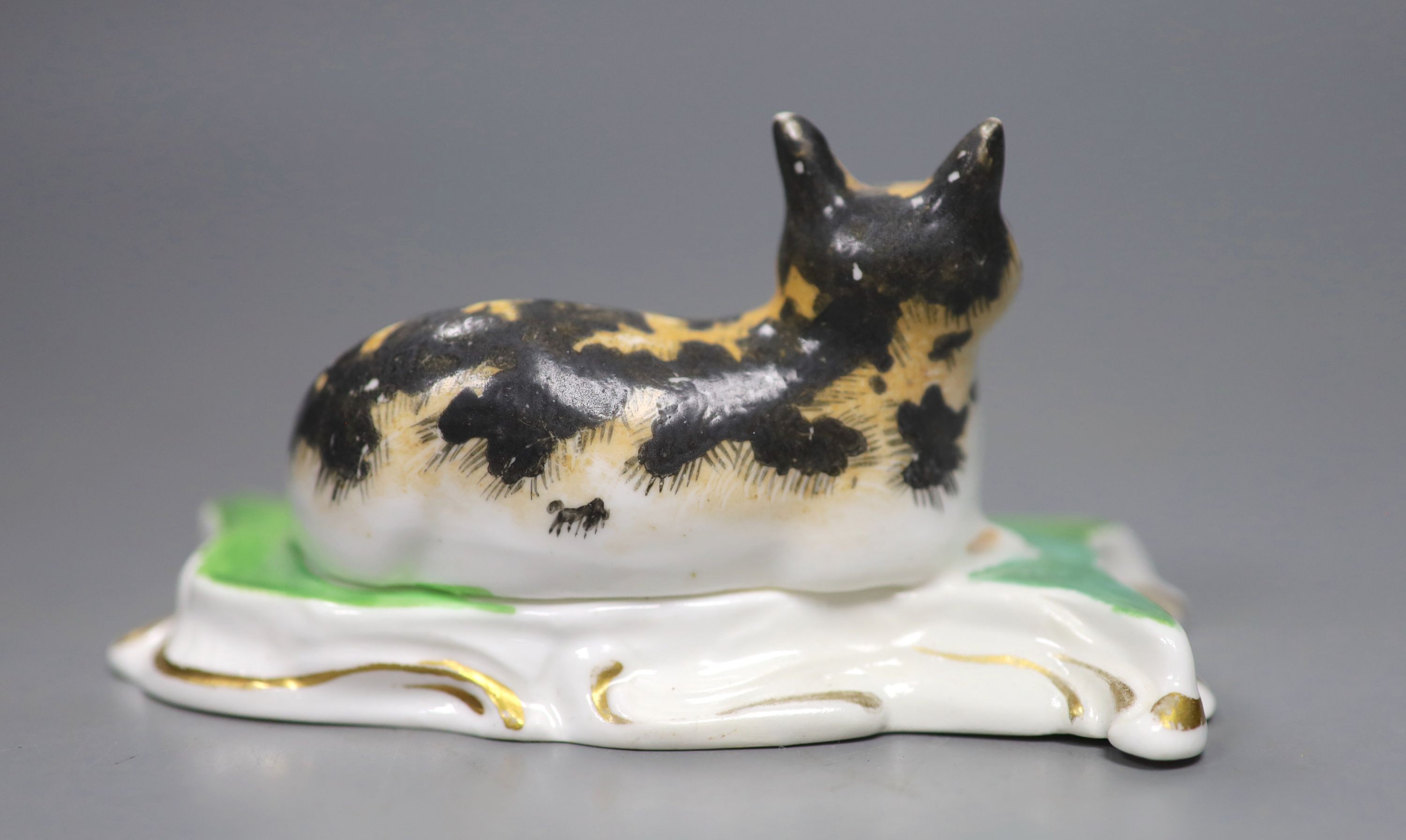 A rare Staffordshire porcelain figure of a recumbent tabby cat, c.1830-50, on a scroll work base, 11.5 cm long